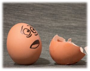 one brown egg with exasperated expression sharpied on the surface appearing to be looking at a broken eggshell